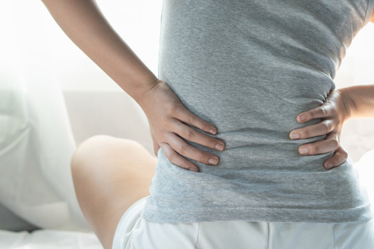 woman sitting in a chiropractic office with touching back due to pain